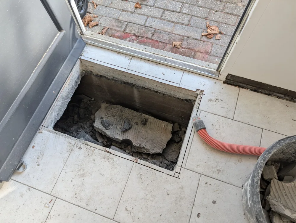 Opening voor een kruipluik in een bestaande tegelvloer bij de voordeur, tijdens het werk
