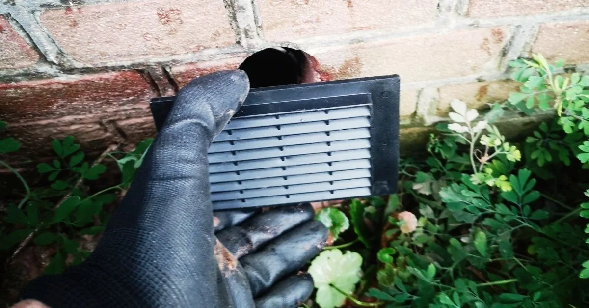 Een zwart kruipruimte ventilatie rooster voor een geboord gat in de gevel